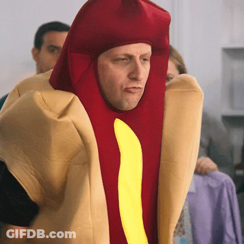 A Man Is Dressed As A Hot Dog With A Yellow Stripe GIF