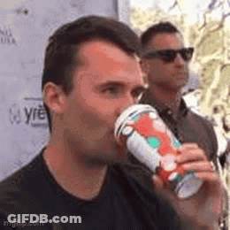 A Man Is Drinking A Cup Of Coffee While Another Man Stands Behind Him . GIF