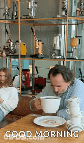 A Man Is Drinking A Cup Of Coffee While Sitting At A Table With Stacks Of Coffee Cups . GIF