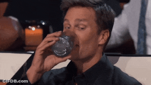 A Man Is Drinking A Glass Of Water With His Mouth Open . GIF