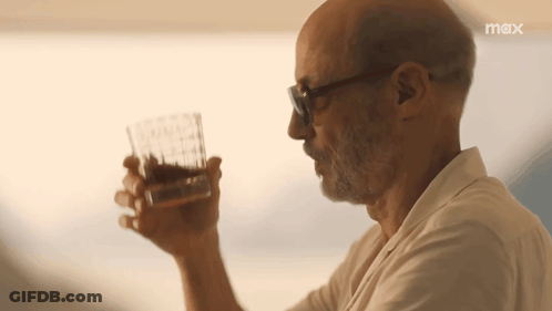 A Man Is Drinking A Glass Of Whiskey With A Max Logo Behind Him GIF