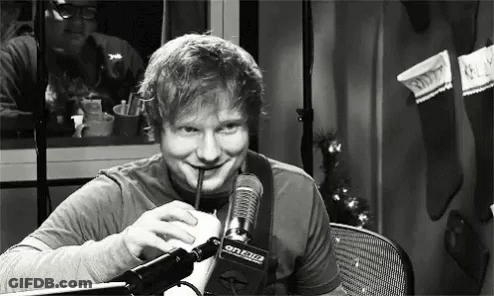 A Man Is Drinking A Milkshake Through A Straw In Front Of A Microphone . GIF