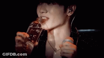 A Man Is Drinking From A Bottle While Holding A Microphone . GIF
