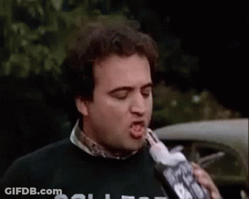 A Man Is Drinking From A Bottle While Wearing A College Sweater . GIF