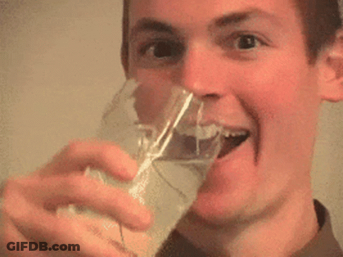 A Man Is Drinking From A Glass And Smiling With His Tongue Out . GIF