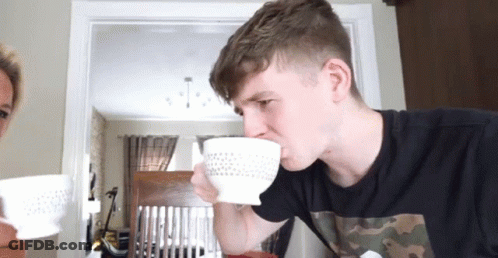 A Man Is Drinking From A White Bowl With A Polka Dot Pattern GIF