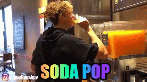A Man Is Drinking Orange Juice From A Soda Pop Machine GIF