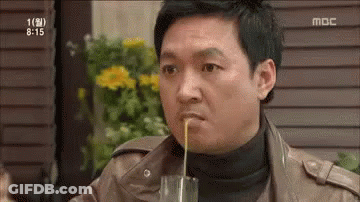A Man Is Drinking Something Through A Straw From A Glass While Sitting At A Table . GIF