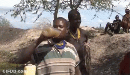 A Man Is Drinking Water From A Bottle While Another Man Sits On A Rock . GIF