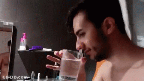 A Man Is Drinking Water From A Glass In A Bathroom . GIF