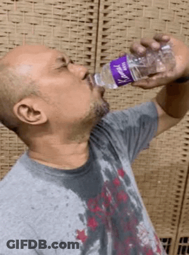 A Man Is Drinking Water From A Plastic Bottle With A Purple Label GIF