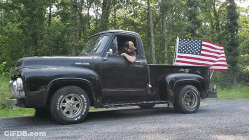 A Man Is Driving A Black Pickup Truck With Dayton Tires GIF