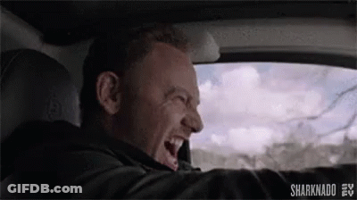 A Man Is Driving A Car And Laughing While Looking Out The Window . GIF