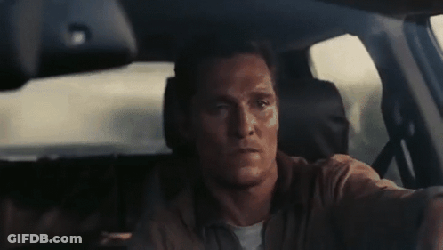 A Man Is Driving A Car And Looking At The Camera . GIF