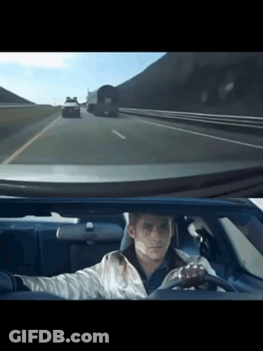 A Man Is Driving A Car On A Highway With A Truck Behind Him GIF