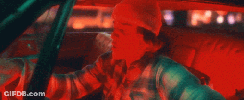 A Man Is Driving A Car With A Beanie On And A Plaid Shirt . GIF