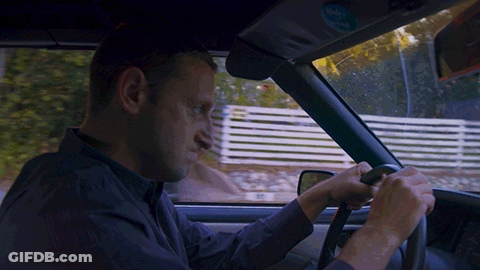 A Man Is Driving A Car With A Sticker On The Rear View Mirror That Says ' Volvo ' GIF