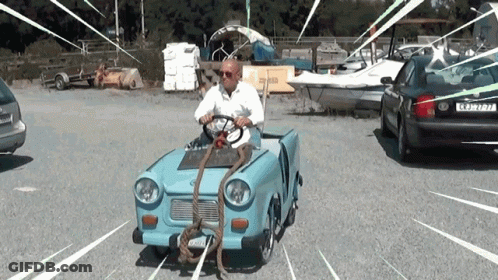 A Man Is Driving A Small Blue Car With A Rope Attached To The Front Of The Car GIF