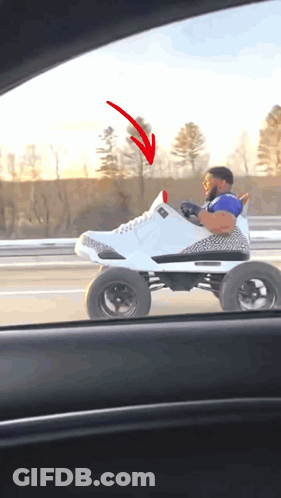 A Man Is Driving A Toy Car That Looks Like A Shoe With A Red Arrow Pointing To It GIF