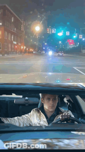 A Man Is Driving Down A Street At Night With A Sign That Says A On It GIF