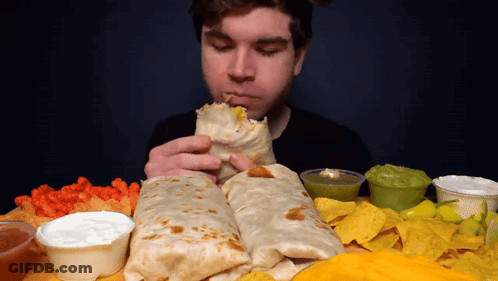 A Man Is Eating A Burrito Surrounded By Nachos And Sauces GIF