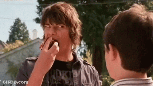 A Man Is Eating A Donut While Another Man Watches . GIF