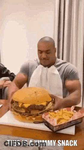 A Man Is Eating A Giant Hamburger And French Fries . GIF