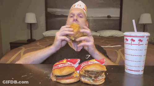 A Man Is Eating A Hamburger Next To A Bag Of Burger King GIF