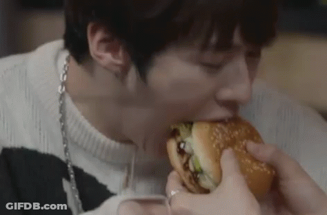 A Man Is Eating A Hamburger With His Eyes Closed . GIF