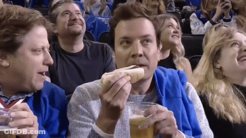 A Man Is Eating A Hot Dog And Drinking Beer While Watching A Game GIF