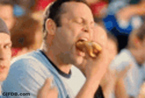 A Man Is Eating A Hot Dog In A Crowd Of People At A Sporting Event . GIF