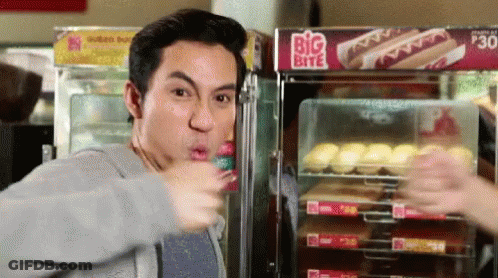 A Man Is Eating A Hot Dog In Front Of A Big Bite Sign GIF