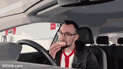 A Man Is Eating A Hot Dog While Driving GIF