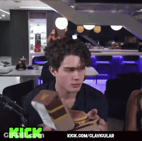 A Man Is Eating A Mcdonald 'S Hamburger In A Restaurant With Kick.com/clavicular On The Bottom GIF