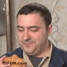 A Man Is Eating A Piece Of Fried Chicken While Looking At The Camera . GIF