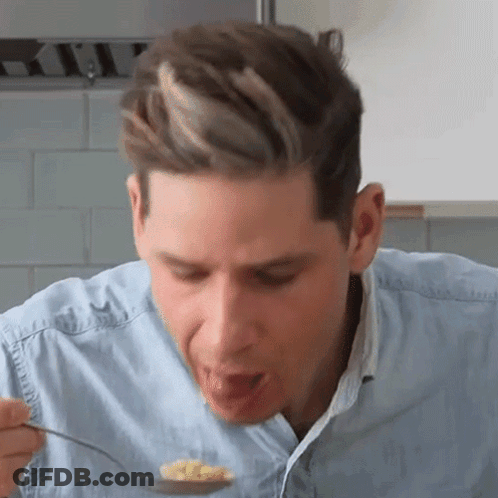 A Man Is Eating Food From A Spoon In A Kitchen . GIF