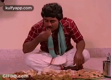 A Man Is Eating Food While Sitting On The Floor . GIF