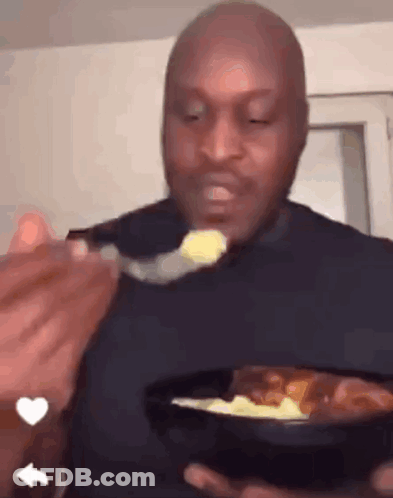 A Man Is Eating Food With A Spoon From A Bowl . GIF