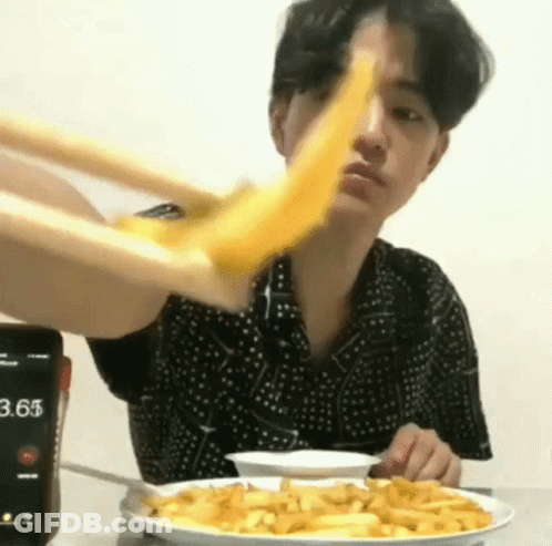 A Man Is Eating French Fries With Chopsticks And A Cell Phone In The Background . GIF
