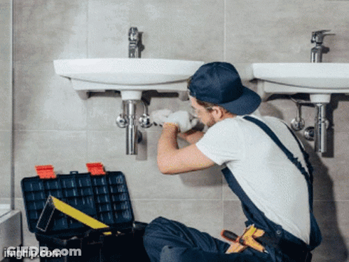 A Man Is Fixing A Sink In A Bathroom With A Toolbox Next To Him GIF