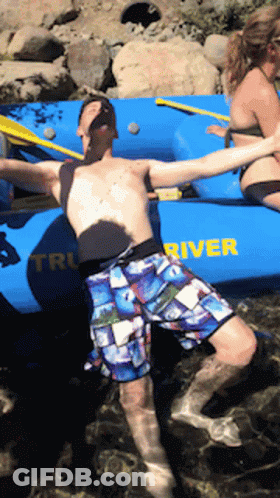 A Man Is Floating In The Water Near A Boat That Says River GIF