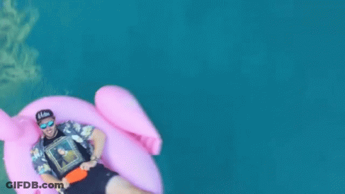 A Man Is Floating On A Pink Flamingo Float In The Water GIF
