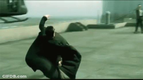 A Man Is Flying Through The Air In Front Of A Helicopter While Wearing A Black Cape . GIF