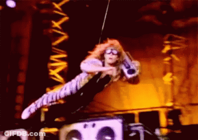 A Man Is Flying Through The Air On A Stage Holding A Microphone . GIF