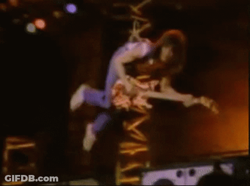 A Man Is Flying Through The Air While Holding A Guitar GIF