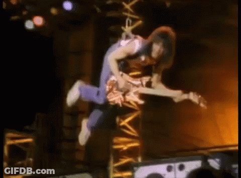 A Man Is Flying Through The Air While Holding A Guitar . GIF