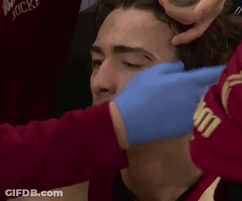 A Man Is Getting A Bandage On His Forehead While Wearing A Red Shirt That Says Hockey GIF
