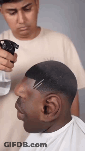 A Man Is Getting His Hair Cut By A Barber While Spraying Water On His Head . GIF