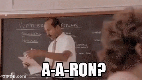 A Man Is Giving A Lecture In Front Of A Blackboard In A Classroom While Holding A Piece Of Paper . GIF