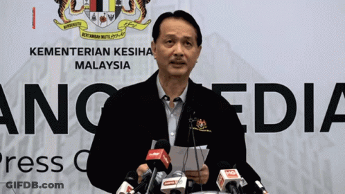 A Man Is Giving A Speech In Front Of A Kementerian Kesihatan Malaysia Sign GIF